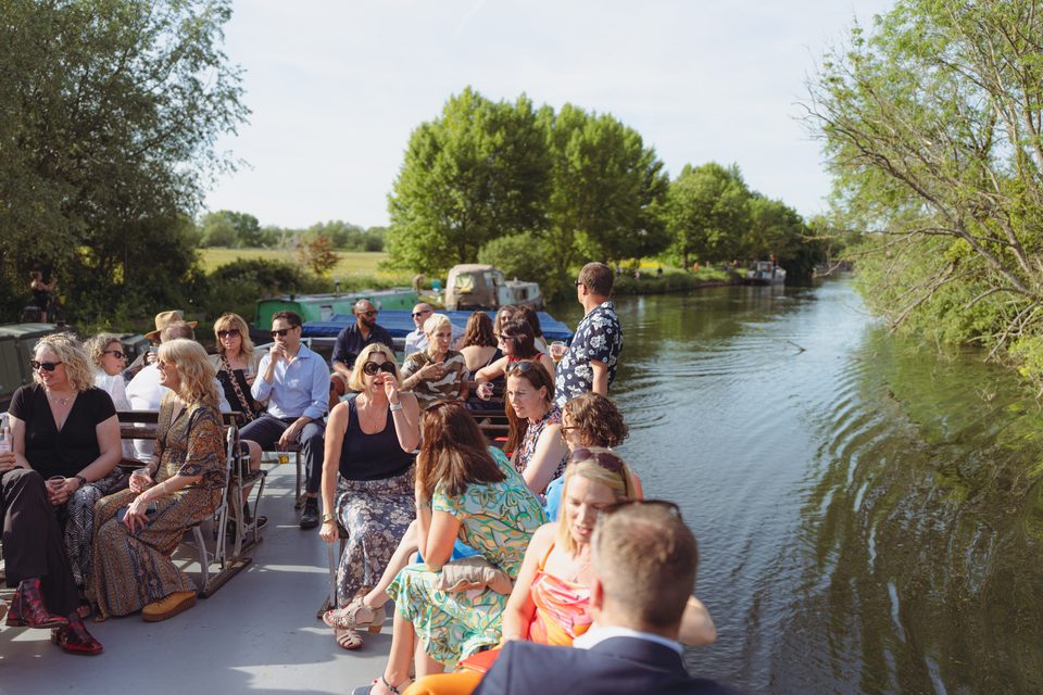 People seated on a boat along a canal, surrounded by greenery and other boats.