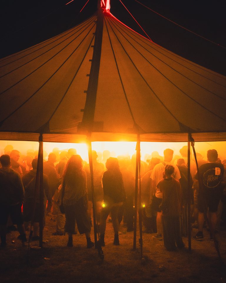 People gathered under a large tent at night, silhouetted against warm interior light.