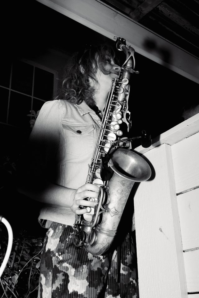 A musician plays saxophone under low-light indoor conditions.