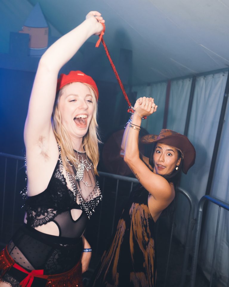 Two women dancing in a dimly lit indoor venue, one with a red hat and the other with a cowboy hat.