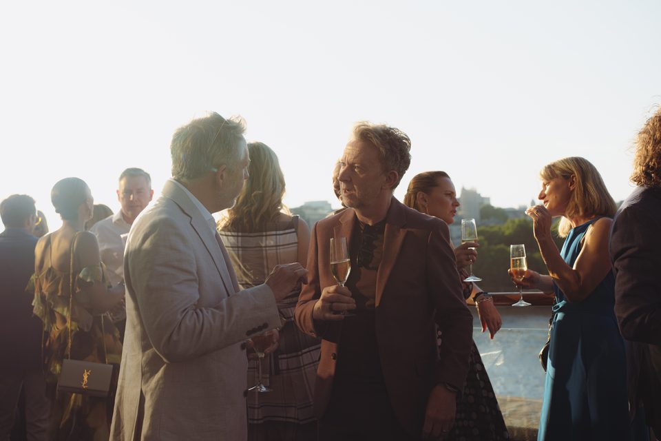 Group of guests conversing under bright sun on an open-air terrace.