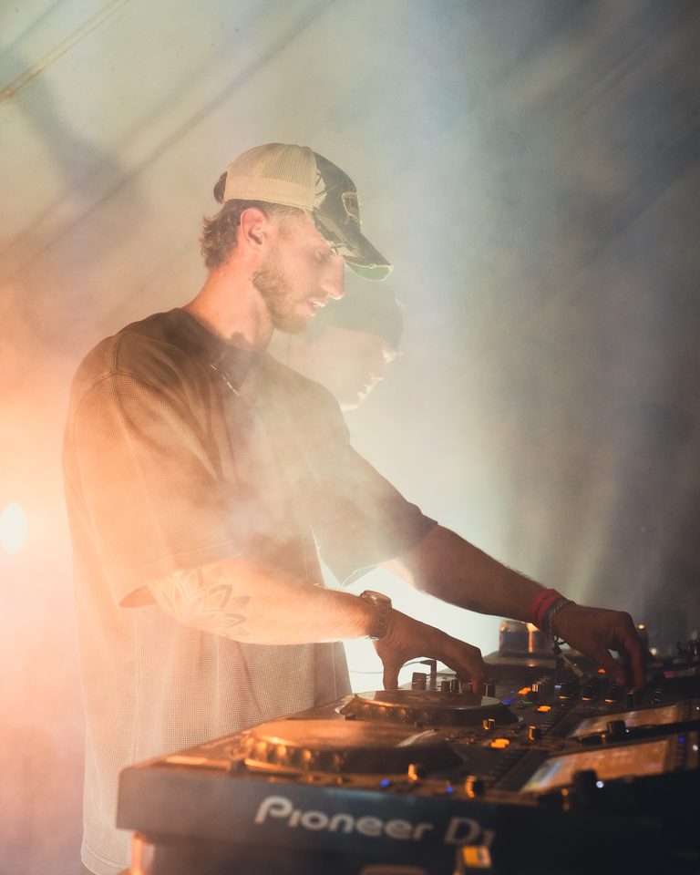 A DJ operating turntables under stage lighting with smoke.