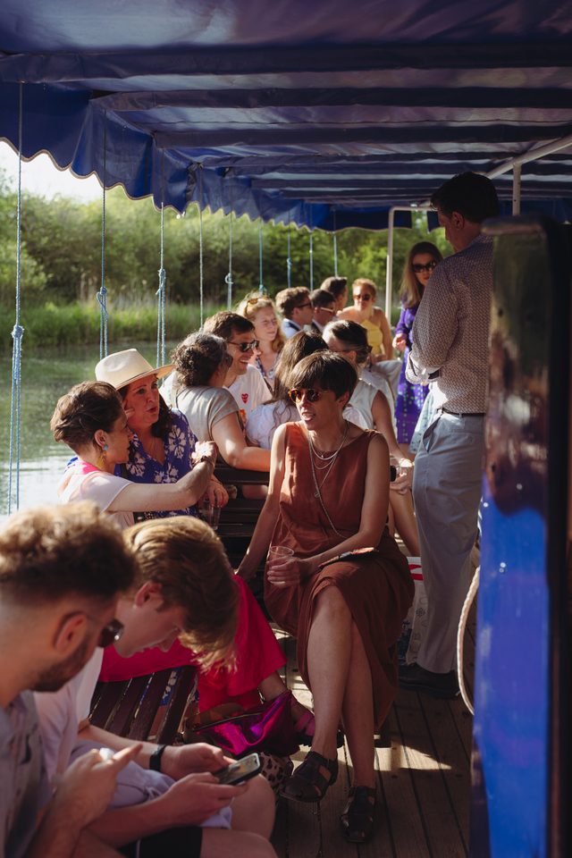People seated under blue canopy on a boat, sunlit, with greenery in background.