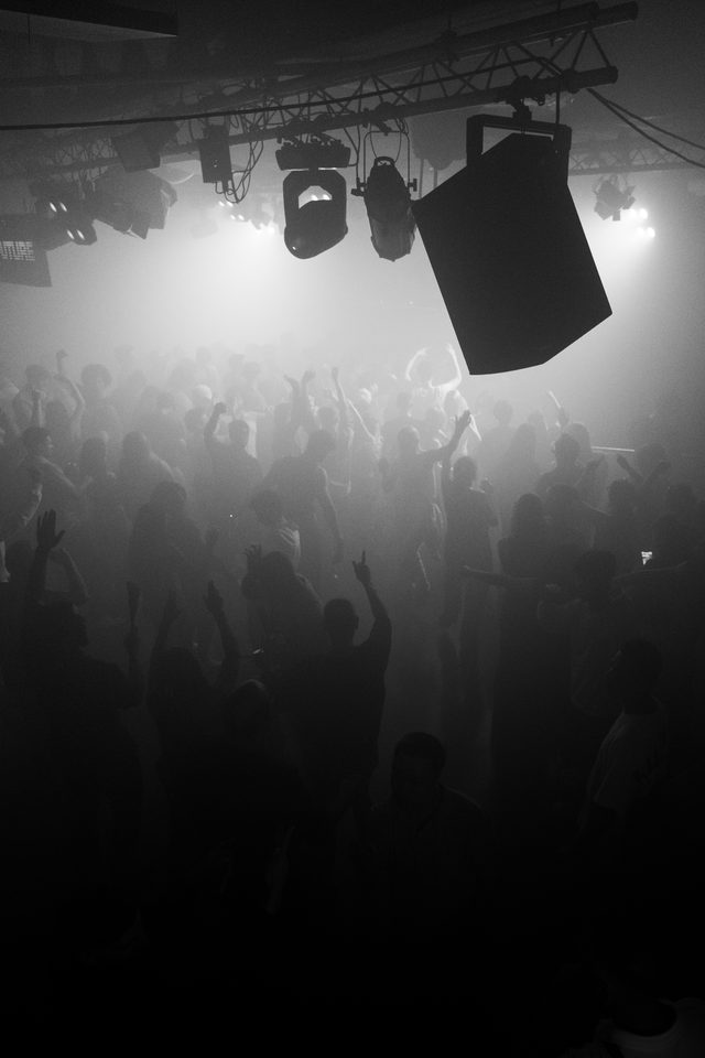 Silhouetted crowd dancing under bright stage lights in a dim club.