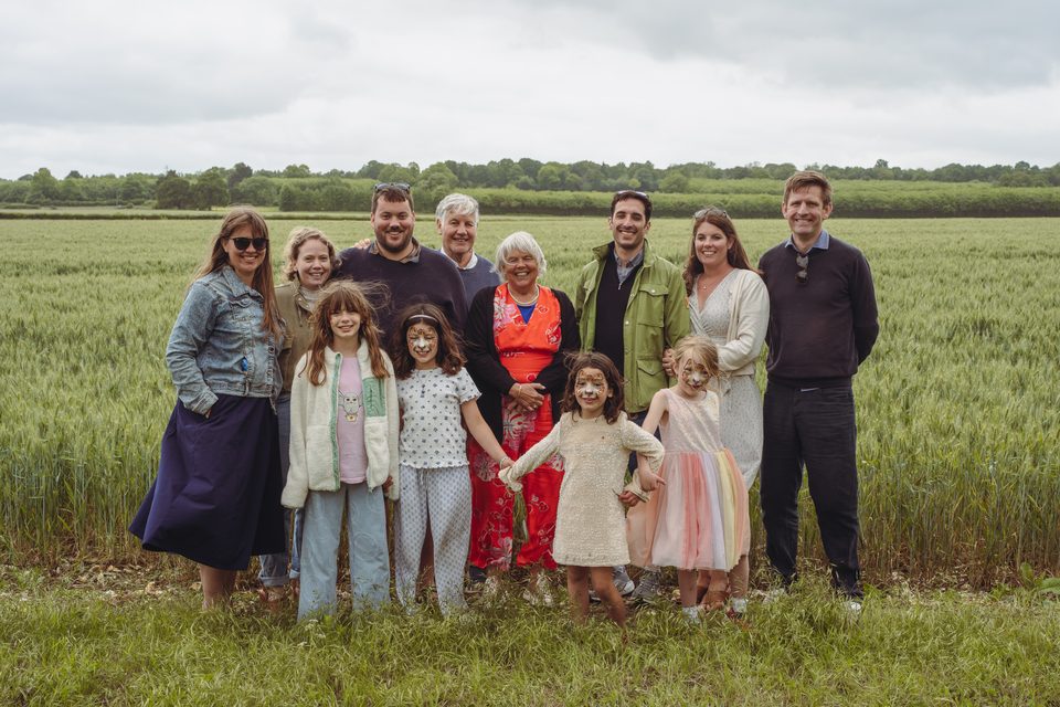Group of adults and children standing in a green field under cloudy sky.