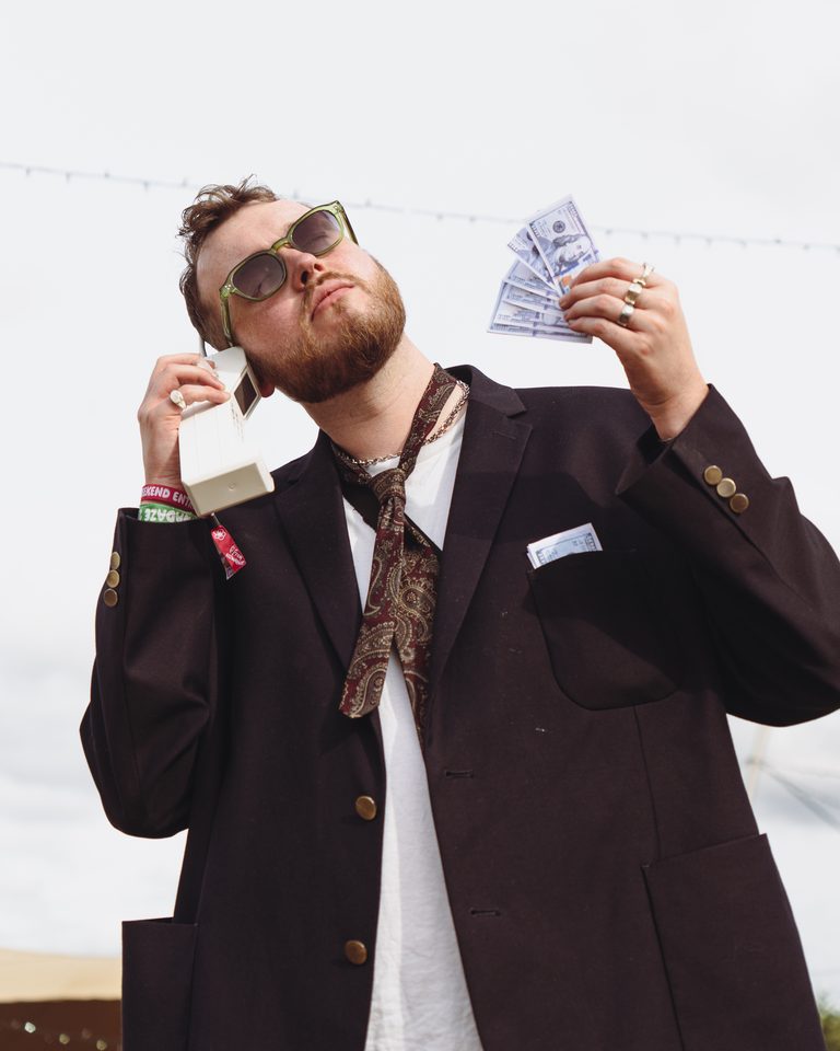 Person in dark suit holding cash and old phone, outdoors under bright sky.