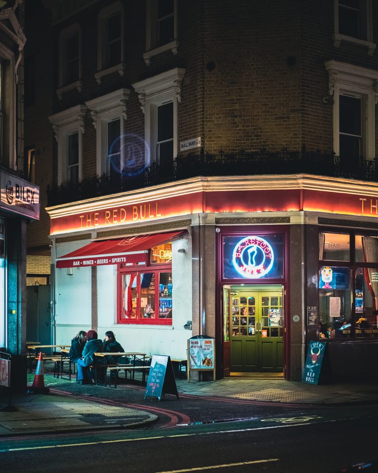 A neon-lit bar corner at night with patrons seated outside.