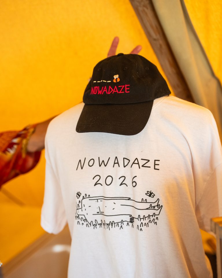 A close-up of a black cap and white t-shirt with 'Nowadaze 2026' text and illustration.