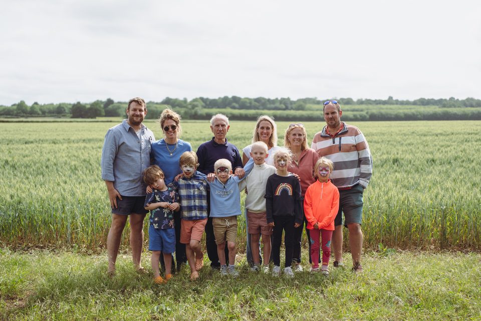 Group of adults and children standing in a green field.