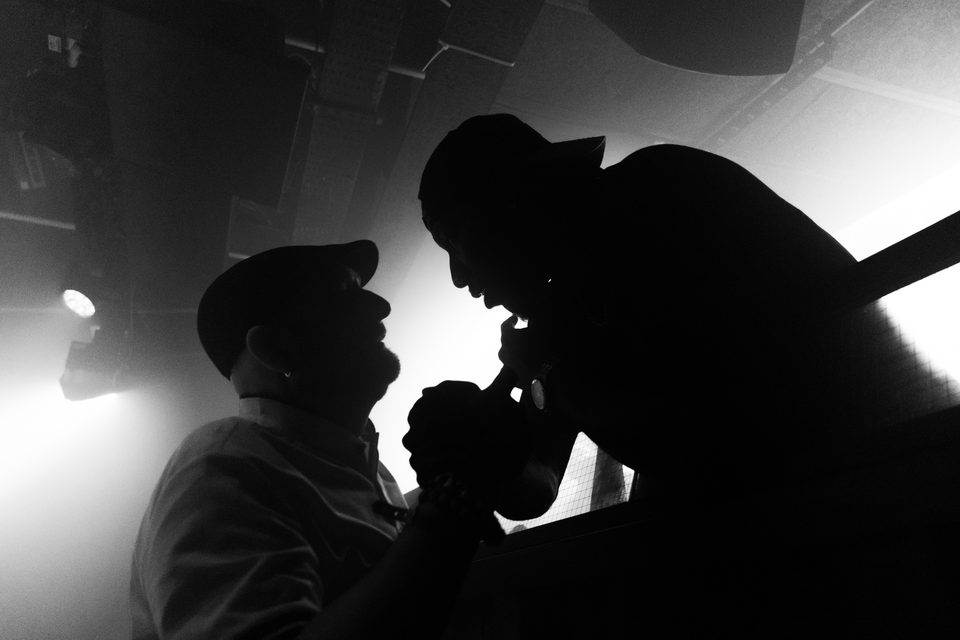 Two figures in silhouette facing each other under stage lighting.