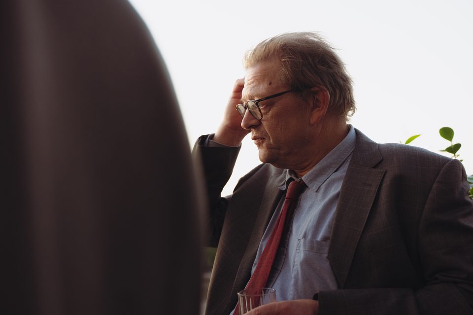 Person in suit and tie, hand on head, backlit, holding glass.