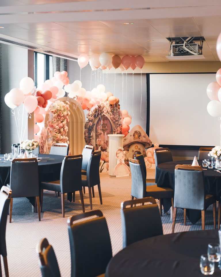 A decorated indoor party space with balloons, floral arches, and fairy-themed decor.