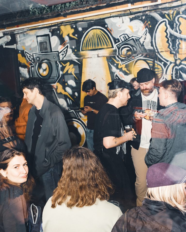 Group of people in a dimly lit indoor club with graffiti wall background.