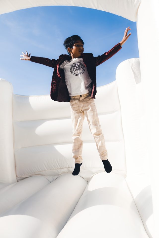 Boy jumping in white inflatable bounce house under clear blue sky.