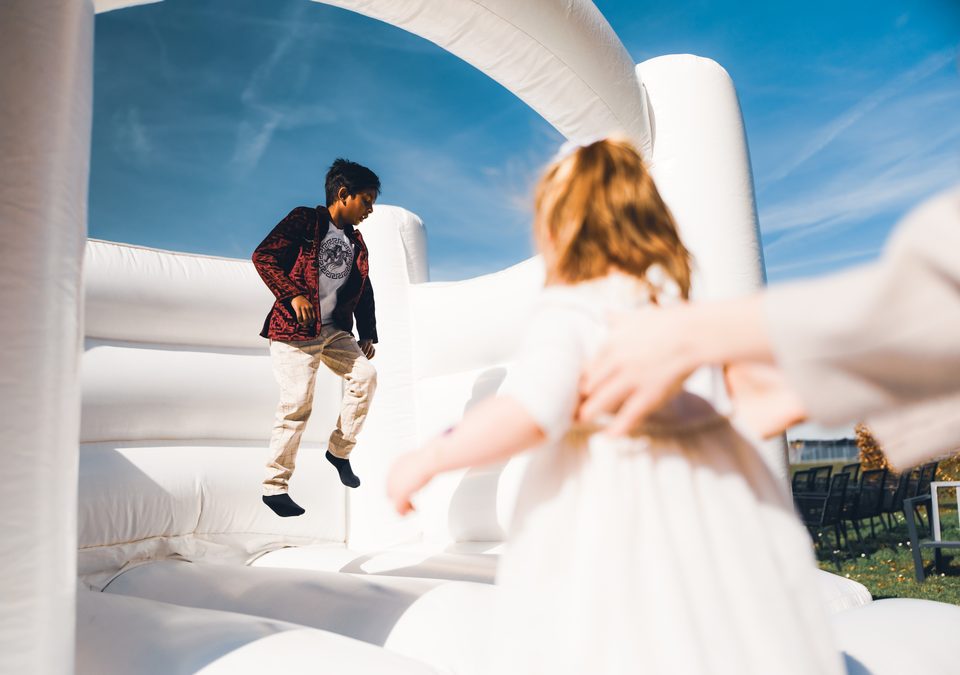 Two children on a white bounce house under clear blue sky.