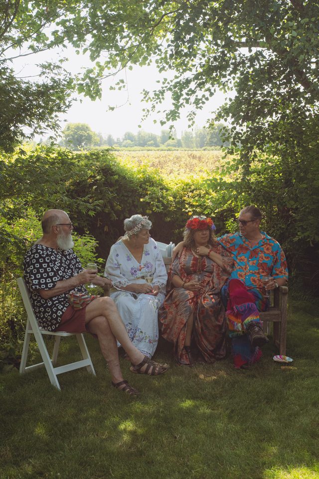 Four people seated outdoors under trees, enjoying drinks in sunlight.