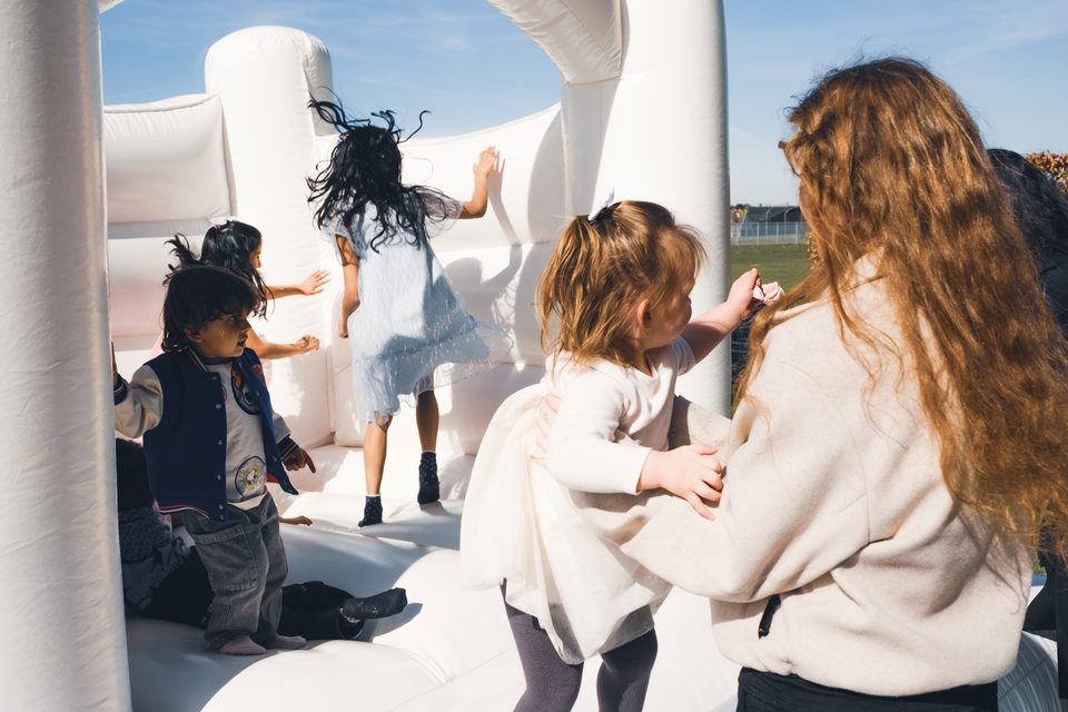 Children playing on a white inflatable bounce house under bright sunlight.