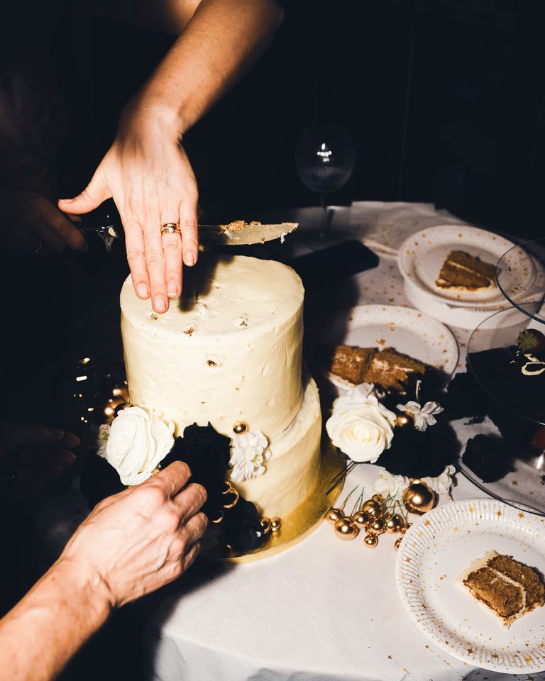 Two hands cutting a two-tiered cake with white and black floral decorations.