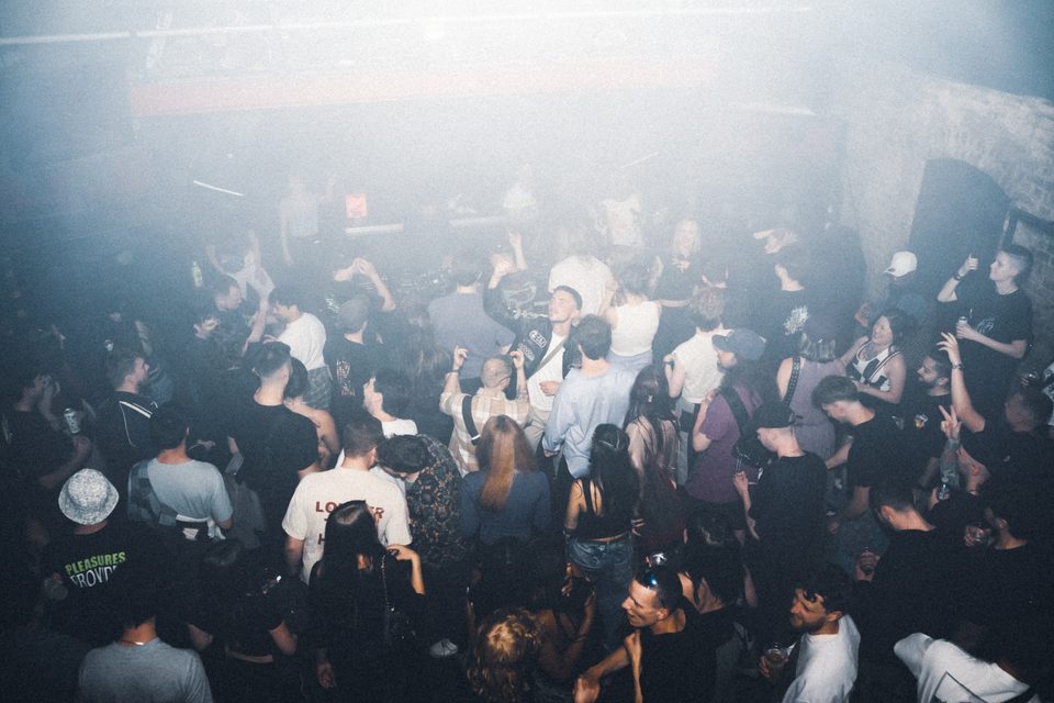 Crowd dancing in smoky club with dim lighting.
