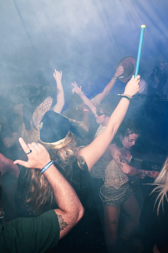 People dancing in a smoky club with blue stage lighting and raised arms.