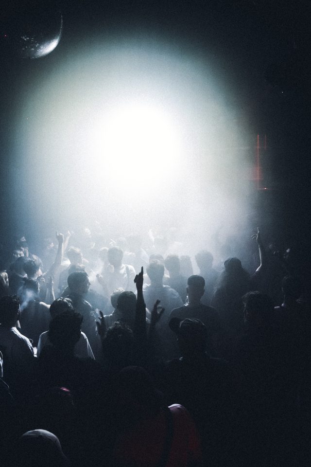 Silhouetted crowd dancing under bright stage light in a dim club.