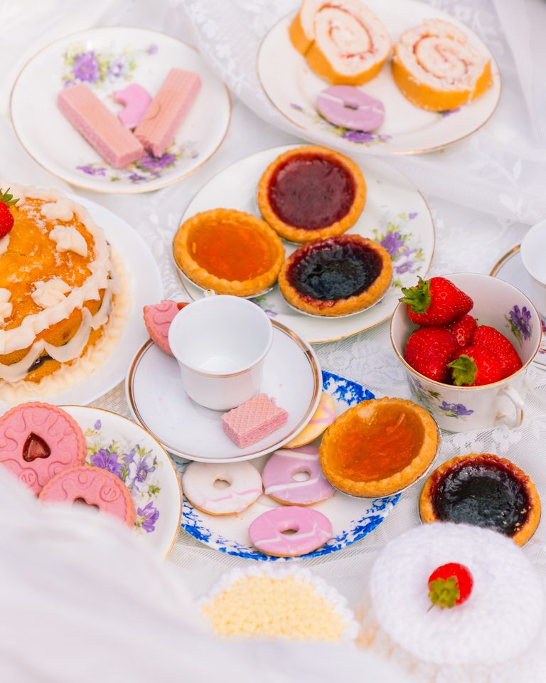 A spread of pastries, tarts, and strawberries on floral plates and cups.