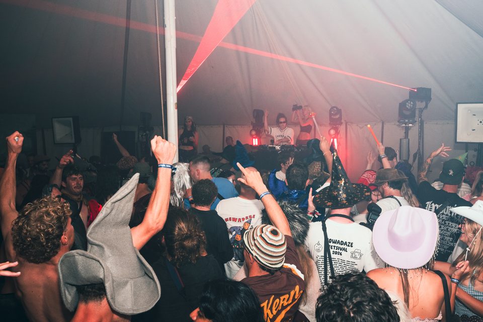 Dense crowd under red laser beams, DJ at booth, indoor festival tent.