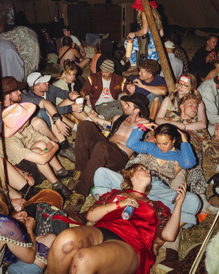 People seated on hay bales under a tent, socializing in low light.