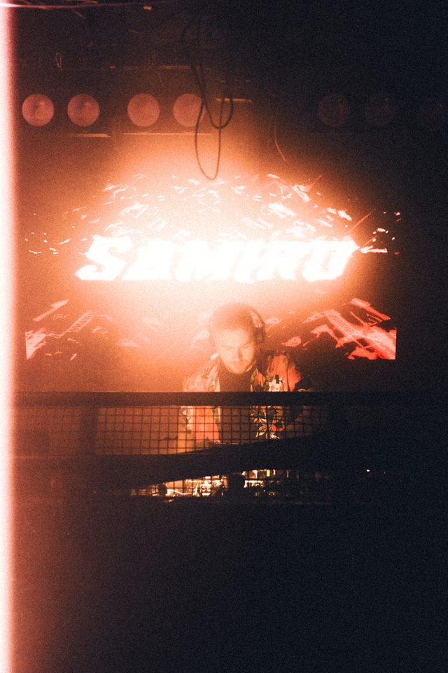 A DJ illuminated by orange stage lights behind a glowing 'SAMURAI' sign.