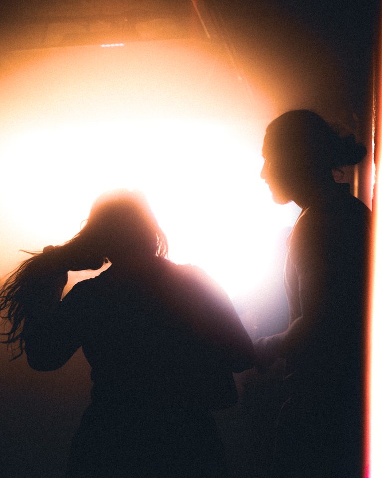 Two figures in silhouette against bright stage light.