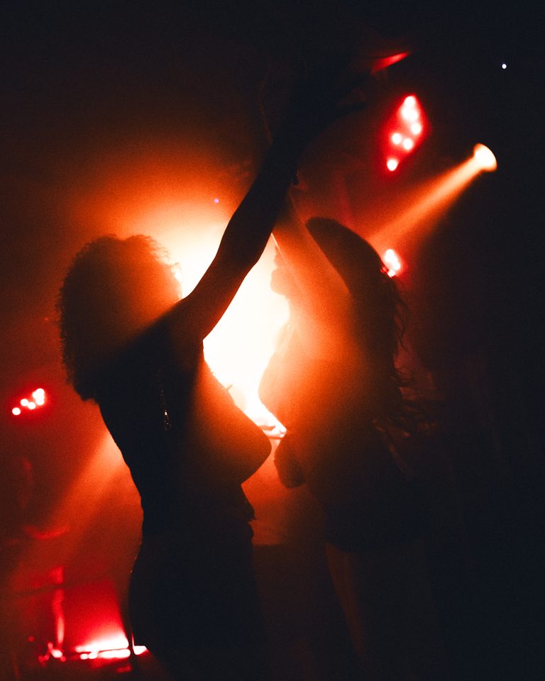 Two figures dancing in red stage light, silhouetted against a bright background.