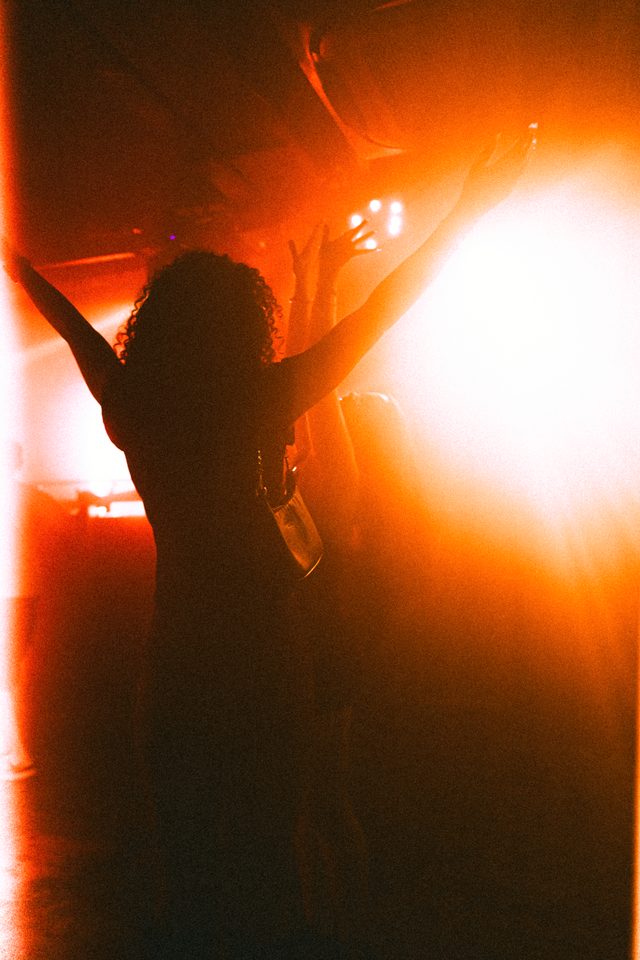 Person dancing with arms raised under bright orange stage lights.