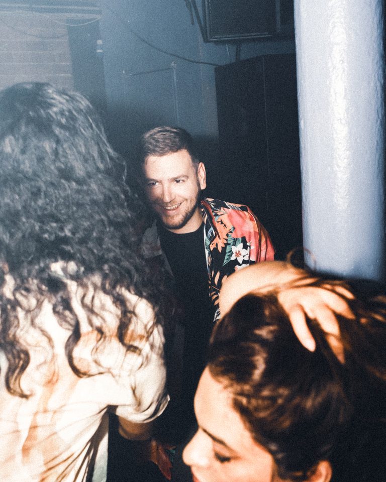 Three people in a dimly lit indoor club, one smiling at the camera.
