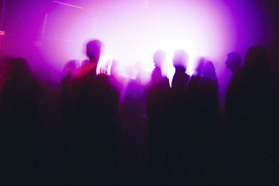 Silhouetted crowd under purple stage lights in a dim indoor club.