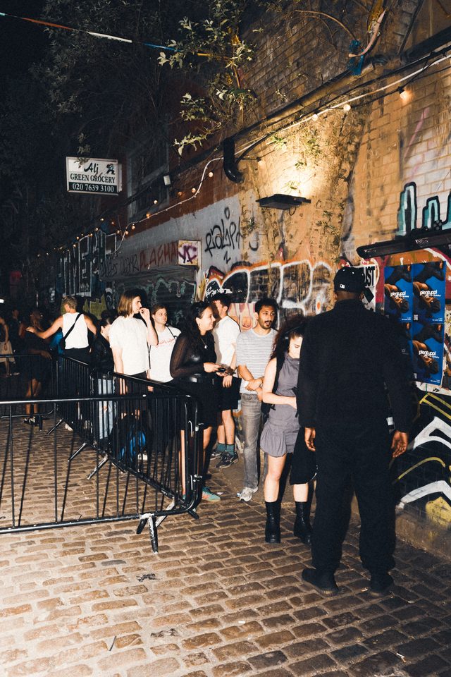 People waiting outside a venue on cobblestone street at night.