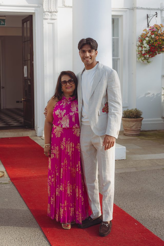 Two individuals standing on a red carpet in front of a white building entrance.