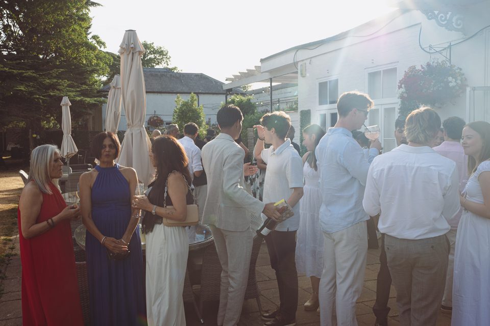 Group of guests mingling under bright sunlight at an outdoor event.