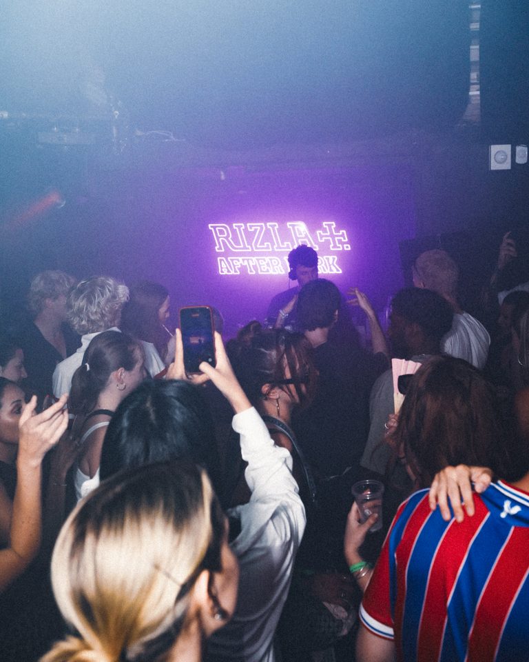 People dancing in a dimly lit club with a glowing sign.
