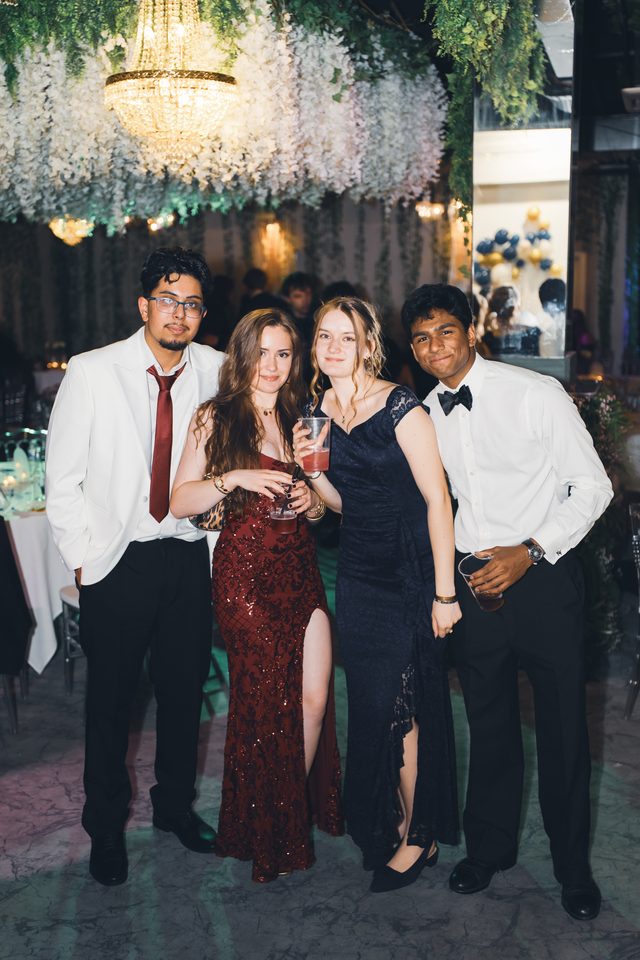 Four people posing together at an indoor event with chandeliers and floral decor.