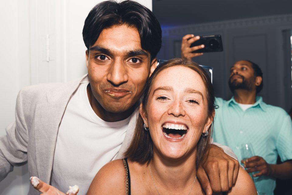 Two people posing for a selfie in a dimly lit indoor venue with a third person in background.