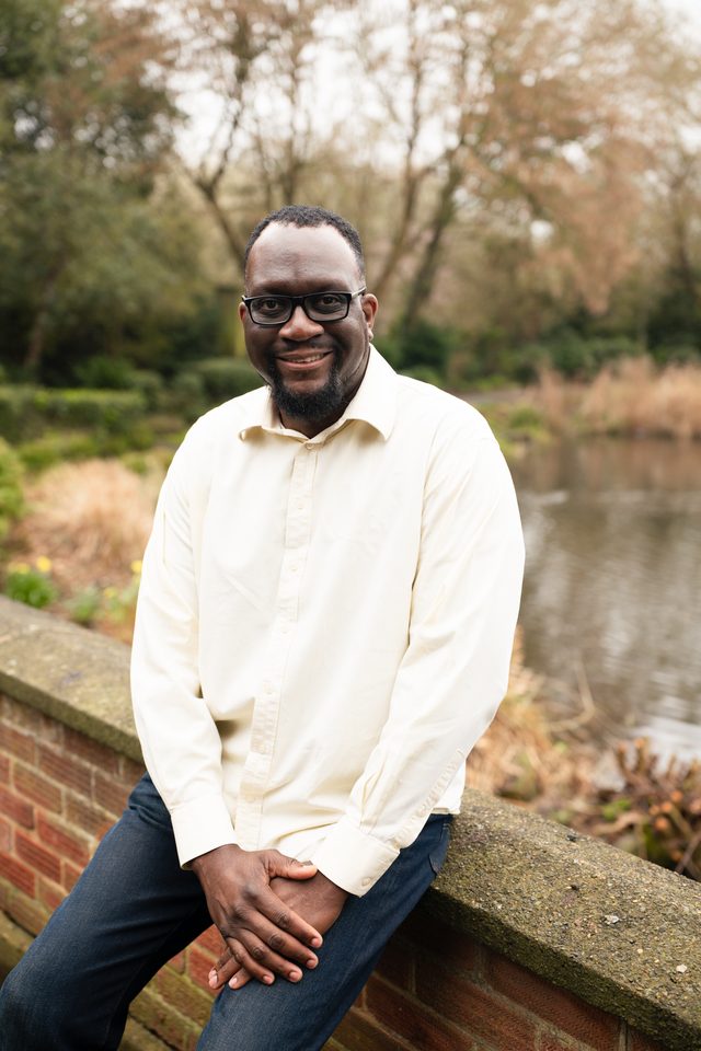 Person in cream shirt sits on stone wall beside water.