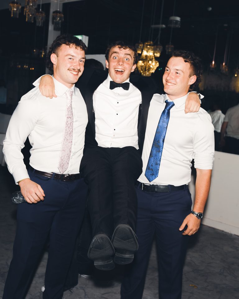 Three men in formal attire posing for a photo in a dimly lit indoor venue.