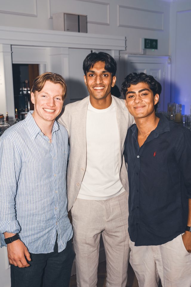 Three men standing close together in a dimly lit indoor space.