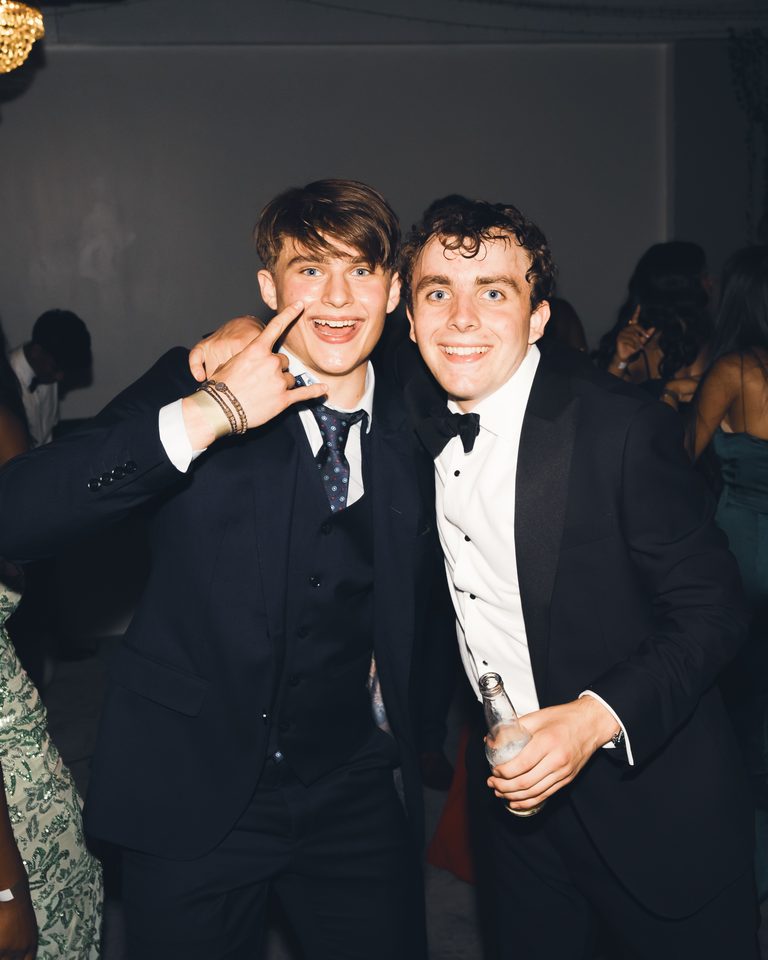 Two men in formal attire posing together at a crowded indoor night event.
