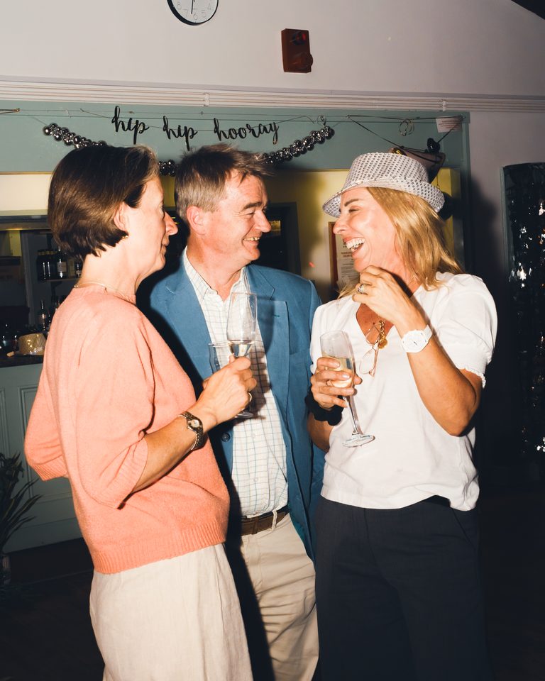 Three people holding champagne glasses, laughing together indoors.