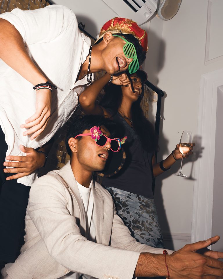 Three people in party attire, one holding a glass, in a dimly lit indoor space.