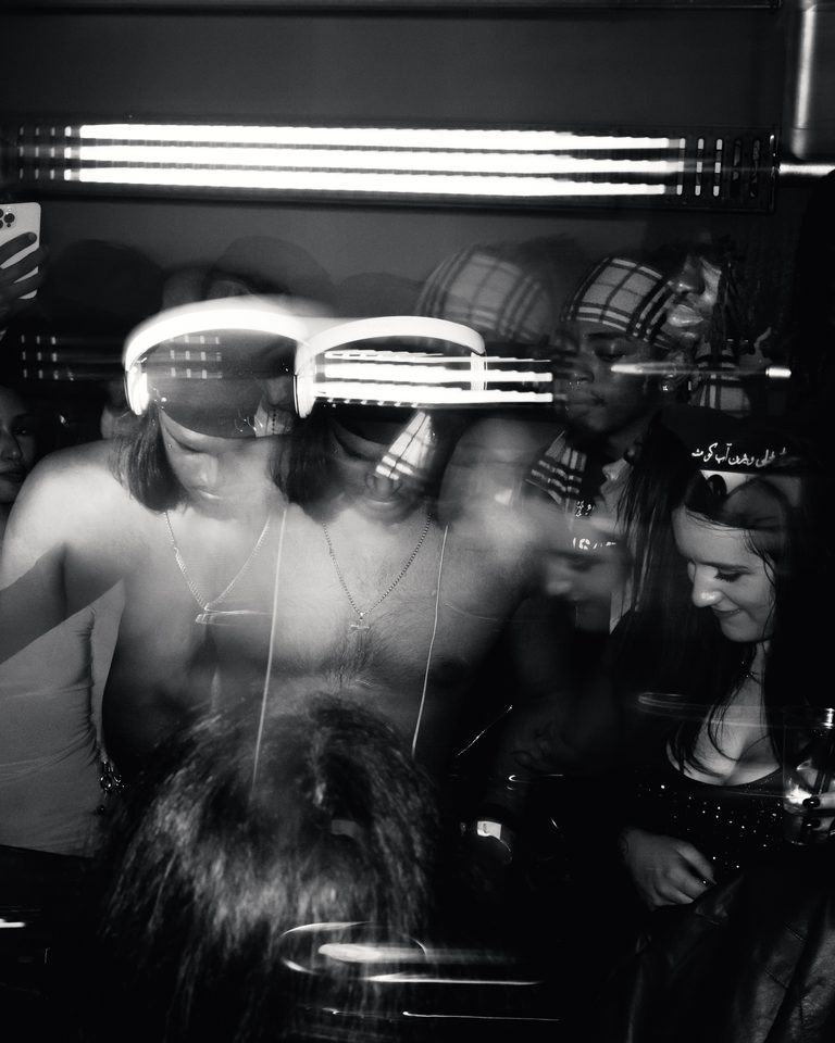 Black and white shot of a crowd in a dimly lit club, blurred motion and overhead lights.