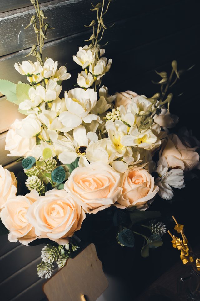 Close-up of artificial white and peach roses with greenery against dark background.