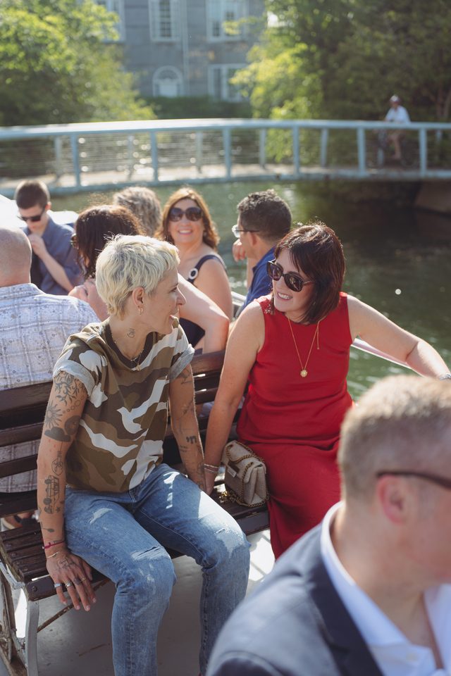 People seated on a boat, smiling and conversing, under bright sunlight.