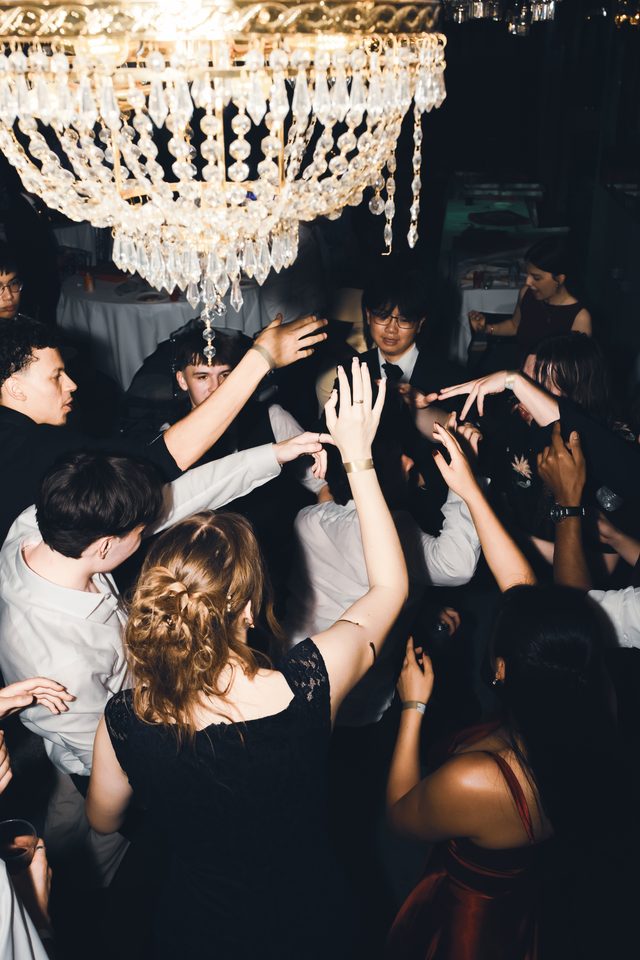 Group of people dancing under a large chandelier in a dimly lit indoor venue.